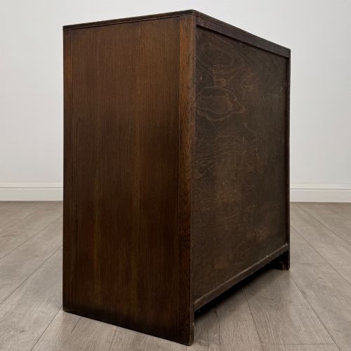 fig 3. A dark oak chest of drawers featuring carved vertical linenfold panels and metallic drop handles.