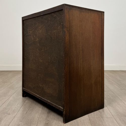 fig 5. A dark oak chest of drawers featuring carved vertical linenfold panels and metallic drop handles.