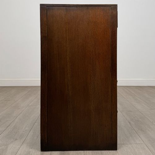 fig 6. A dark oak chest of drawers featuring carved vertical linenfold panels and metallic drop handles.