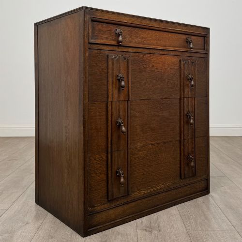fig 7. A dark oak chest of drawers featuring carved vertical linenfold panels and metallic drop handles.
