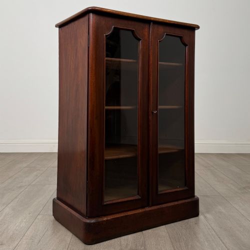 fig 8. A nineteenth-century mahogany display cabinet featuring twin glazed doors with arched framing and a plinth base.