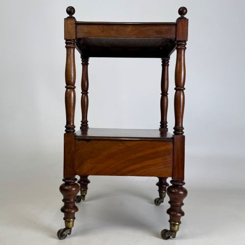 fig 2. A Victorian mahogany two-tiered stand featuring turned corner supports, top finials, a lower single drawer with a round wooden knob, and brass castors.