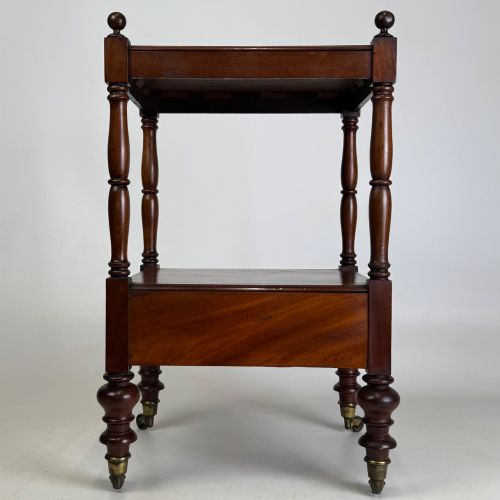 fig 4. A Victorian mahogany two-tiered stand featuring turned corner supports, top finials, a lower single drawer with a round wooden knob, and brass castors.