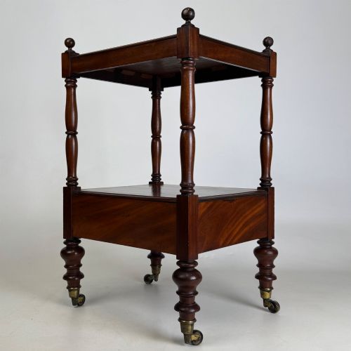 fig 5. A Victorian mahogany two-tiered stand featuring turned corner supports, top finials, a lower single drawer with a round wooden knob, and brass castors.