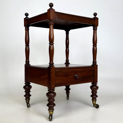 fig 7. A Victorian mahogany two-tiered stand featuring turned corner supports, top finials, a lower single drawer with a round wooden knob, and brass castors.
