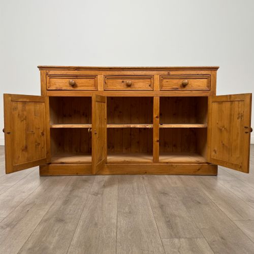 fig 1. A vintage pine farmhouse sideboard featuring three frieze drawers above three panelled cupboard doors with turned wooden knobs on a plinth base.