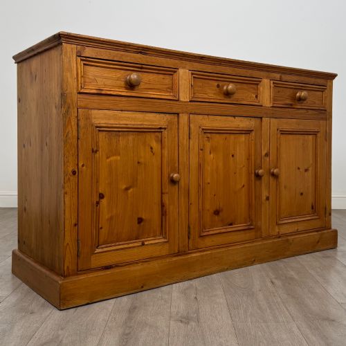 fig 8. A vintage pine farmhouse sideboard featuring three frieze drawers above three panelled cupboard doors with turned wooden knobs on a plinth base.