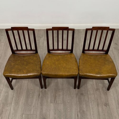 fig 7. A set of six antique mahogany dining chairs featuring vertical slat backs, square legs, and olive green leather seats finished with brass studs.