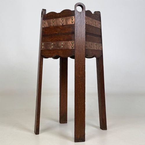 fig 1. An antique Arts and Crafts dark oak plant stand featuring copper straps with brass rivets, pierced handles, and scalloped edges.