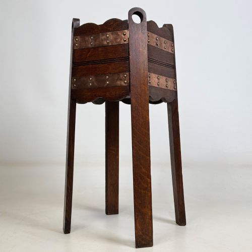 fig 3. An antique Arts and Crafts dark oak plant stand featuring copper straps with brass rivets, pierced handles, and scalloped edges.