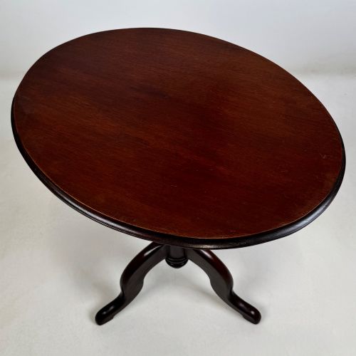 fig 4. An antique dark mahogany side table featuring a smooth oval top, a centrally turned pedestal stem, and three splayed tripod legs.