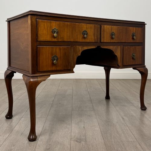 fig 7. A 20th-century walnut writing table featuring four drawers, decorative brass drop handles, an arched kneehole centre, and curved cabriole legs.