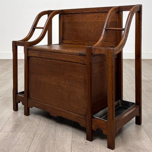 fig 1. An antique Edwardian golden oak hall seat featuring a central panelled backrest and integrated side umbrella stands with metal drip trays.
