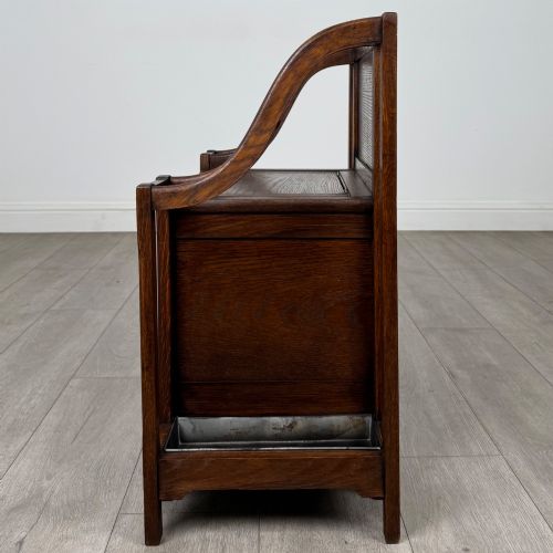 fig 2. An antique Edwardian golden oak hall seat featuring a central panelled backrest and integrated side umbrella stands with metal drip trays.