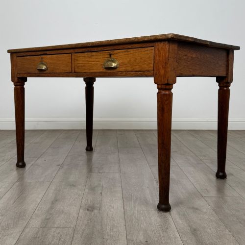 fig 1. An antique early 20th-century oak writing table featuring two front drawers with brass cup handles and turned legs.