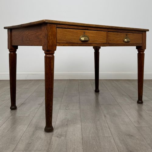 fig 7. An antique early 20th-century oak writing table featuring two front drawers with brass cup handles and turned legs.
