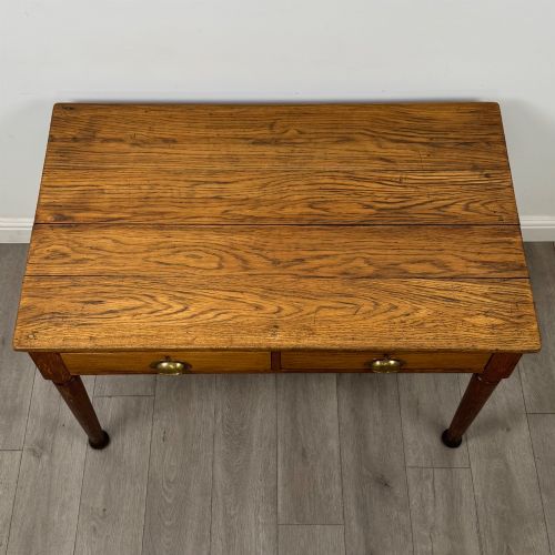 fig 8. An antique early 20th-century oak writing table featuring two front drawers with brass cup handles and turned legs.