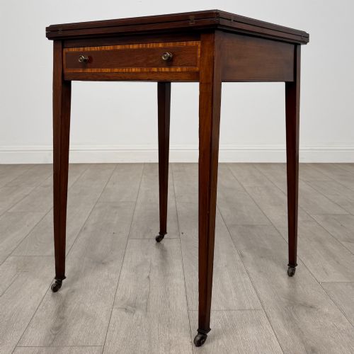 fig 1. An Edwardian mahogany envelope card table with crossbanded satinwood inlay, a single drawer, and tapered square legs on brass castors.