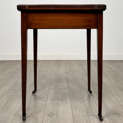 fig 2. An Edwardian mahogany envelope card table with crossbanded satinwood inlay, a single drawer, and tapered square legs on brass castors.