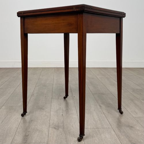 fig 3. An Edwardian mahogany envelope card table with crossbanded satinwood inlay, a single drawer, and tapered square legs on brass castors.