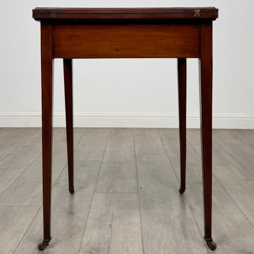 fig 4. An Edwardian mahogany envelope card table with crossbanded satinwood inlay, a single drawer, and tapered square legs on brass castors.