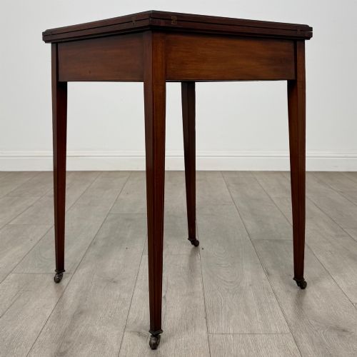 fig 5. An Edwardian mahogany envelope card table with crossbanded satinwood inlay, a single drawer, and tapered square legs on brass castors.