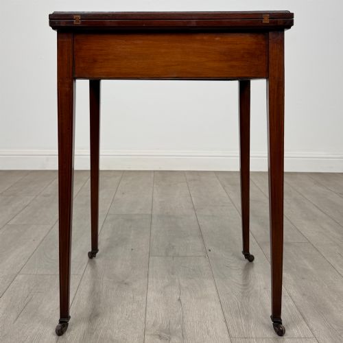 fig 6. An Edwardian mahogany envelope card table with crossbanded satinwood inlay, a single drawer, and tapered square legs on brass castors.
