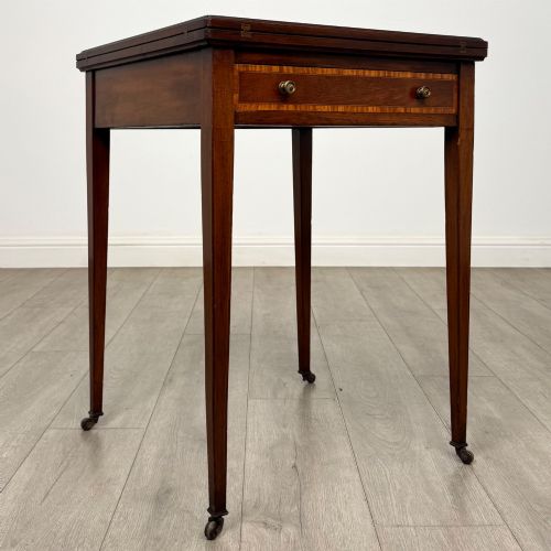 fig 7. An Edwardian mahogany envelope card table with crossbanded satinwood inlay, a single drawer, and tapered square legs on brass castors.
