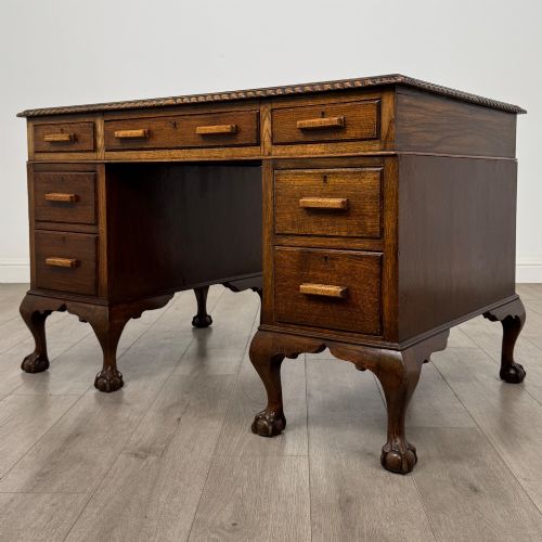 fig 1. An antique oak pedestal desk featuring twin drawer pedestals, carved borders, and cabriole legs terminating in ball-and-claw feet.