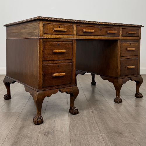 fig 7. An antique oak pedestal desk featuring twin drawer pedestals, carved borders, and cabriole legs terminating in ball-and-claw feet.