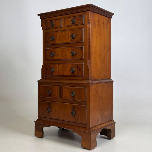 fig 1. A small yew wood chest of drawers featuring a stepped tallboy structure with brass ring handles and bracket feet.