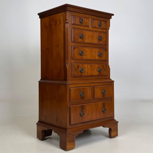 fig 7. A small yew wood chest of drawers featuring a stepped tallboy structure with brass ring handles and bracket feet.