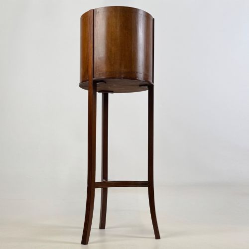 fig 3. A tall Edwardian mahogany plant stand featuring a cylindrical top bucket with subtle line inlay, supported by three elongated curved legs and a triangular lower shelf.