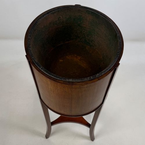 fig 4. A tall Edwardian mahogany plant stand featuring a cylindrical top bucket with subtle line inlay, supported by three elongated curved legs and a triangular lower shelf.