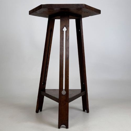 fig 2. An antique dark oak Arts and Crafts side table featuring a hexagonal top, three splayed legs with pierced cutouts, and a lower triangular shelf.