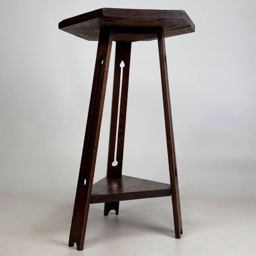 fig 3. An antique dark oak Arts and Crafts side table featuring a hexagonal top, three splayed legs with pierced cutouts, and a lower triangular shelf.