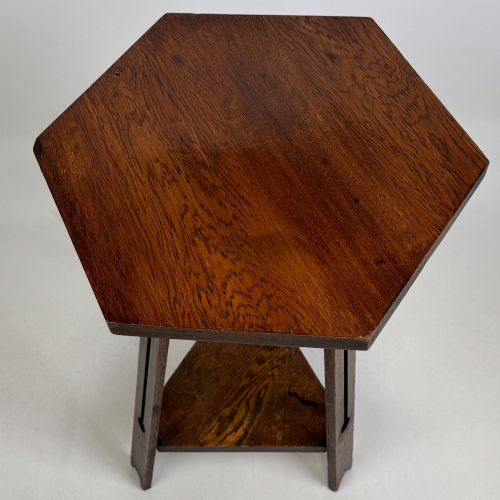 fig 4. An antique dark oak Arts and Crafts side table featuring a hexagonal top, three splayed legs with pierced cutouts, and a lower triangular shelf.