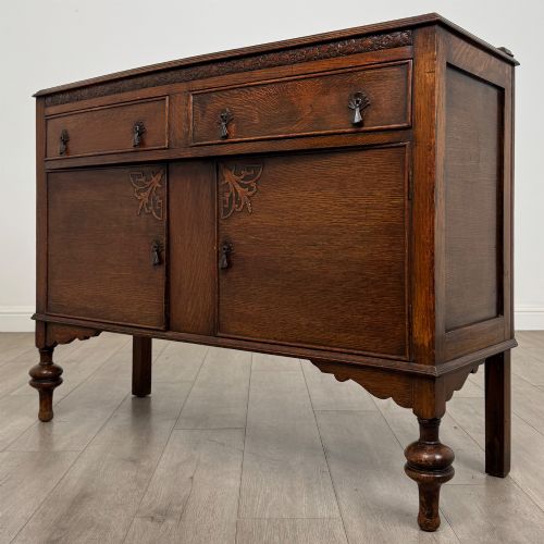 fig 2. A dark oak sideboard featuring two carved drawers above a double-door cupboard resting on turned legs.