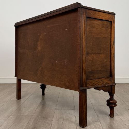 fig 6. A dark oak sideboard featuring two carved drawers above a double-door cupboard resting on turned legs.