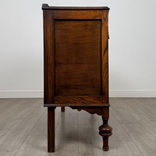 fig 7. A dark oak sideboard featuring two carved drawers above a double-door cupboard resting on turned legs.
