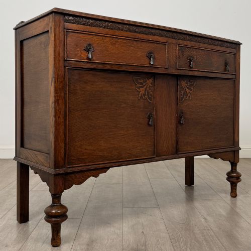 fig 8. A dark oak sideboard featuring two carved drawers above a double-door cupboard resting on turned legs.