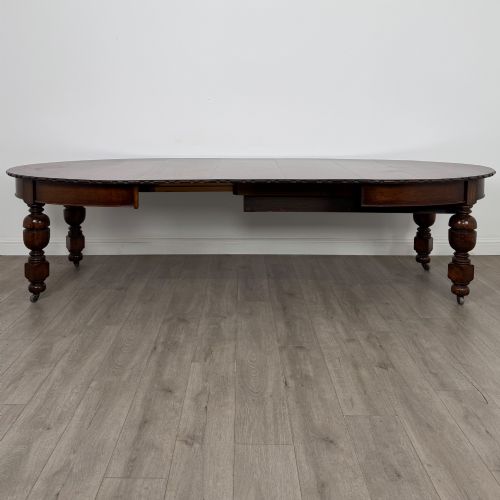 fig 1. A large antique Edwardian extending oak dining table with detailed carved borders, thick turned legs, and brass castors.