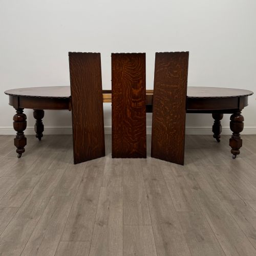 fig 3. A large antique Edwardian extending oak dining table with detailed carved borders, thick turned legs, and brass castors.