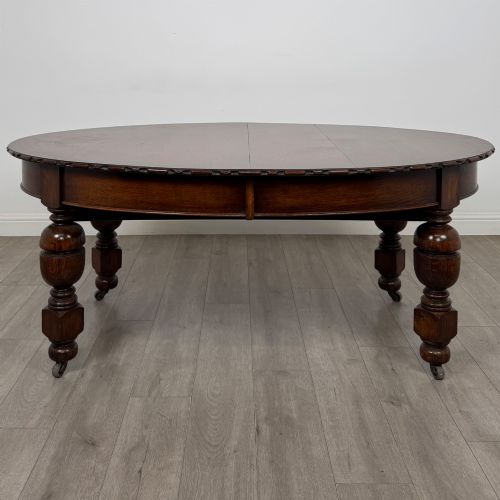 fig 5. A large antique Edwardian extending oak dining table with detailed carved borders, thick turned legs, and brass castors.