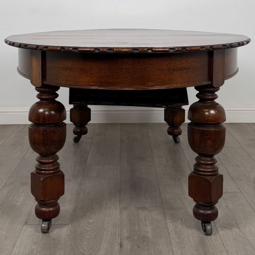 fig 6. A large antique Edwardian extending oak dining table with detailed carved borders, thick turned legs, and brass castors.