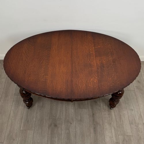 fig 7. A large antique Edwardian extending oak dining table with detailed carved borders, thick turned legs, and brass castors.