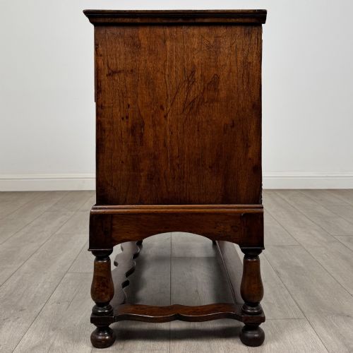 fig 2. An antique 19th-century William and Mary style walnut chest of drawers featuring two deep drawers with ornate brass drop handles, raised on turned legs connected by a wavy stretcher base.