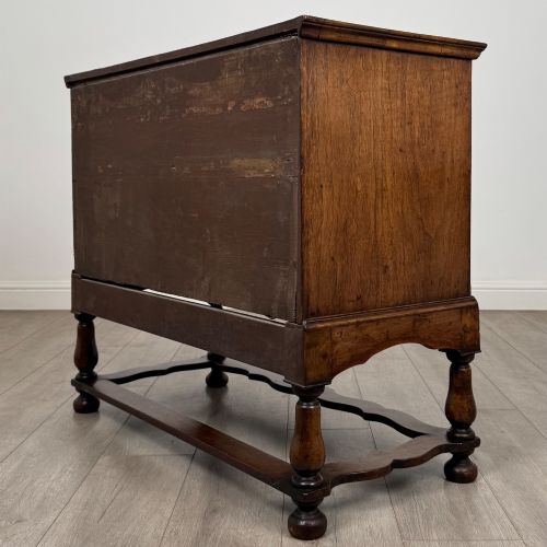 fig 5. An antique 19th-century William and Mary style walnut chest of drawers featuring two deep drawers with ornate brass drop handles, raised on turned legs connected by a wavy stretcher base.