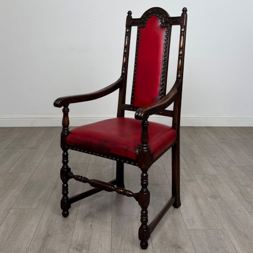 fig 1. A set of six dark oak dining chairs featuring red leather upholstery, carved crests, turned legs, and brass stud trimming.