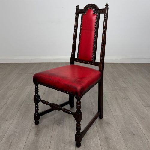 fig 2. A set of six dark oak dining chairs featuring red leather upholstery, carved crests, turned legs, and brass stud trimming.